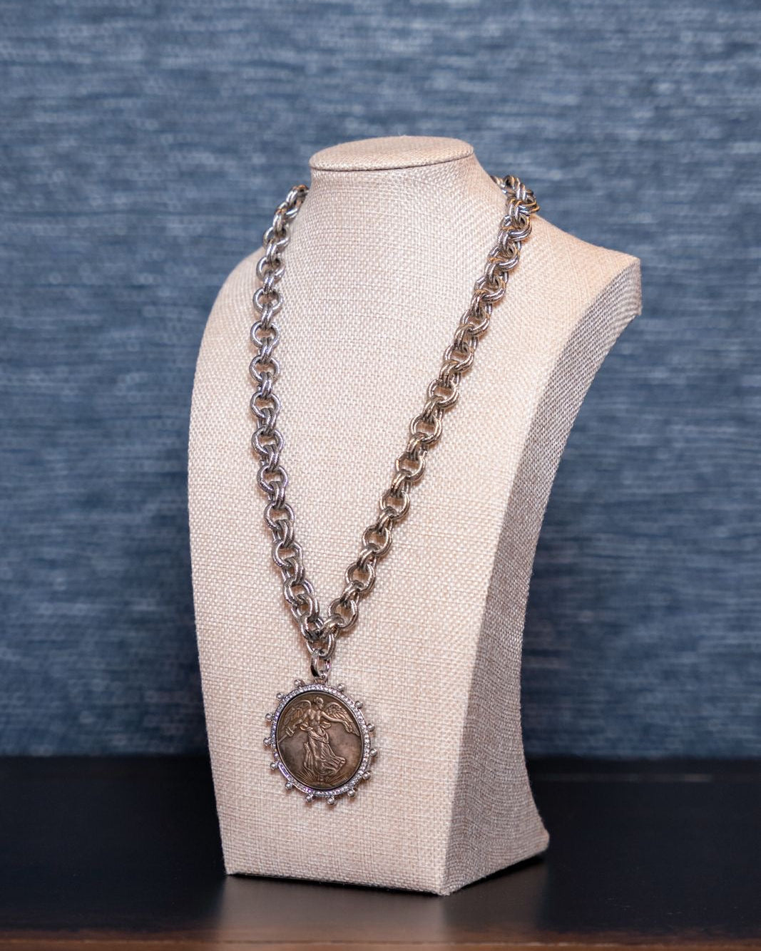 Silver necklace with a pendant on a mannequin bust against a blue textured background