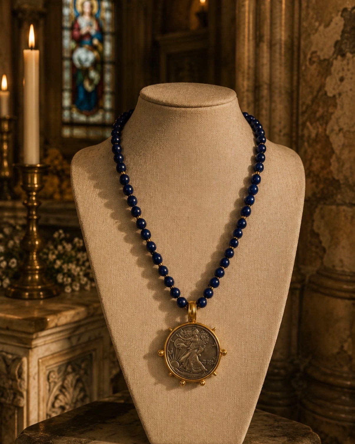 A beaded necklace with deep blue beads and a gold-toned oval pendant featuring an embossed figure, displayed on a beige mannequin bust in a softly lit church interior with candles and stone architecture in the background.
