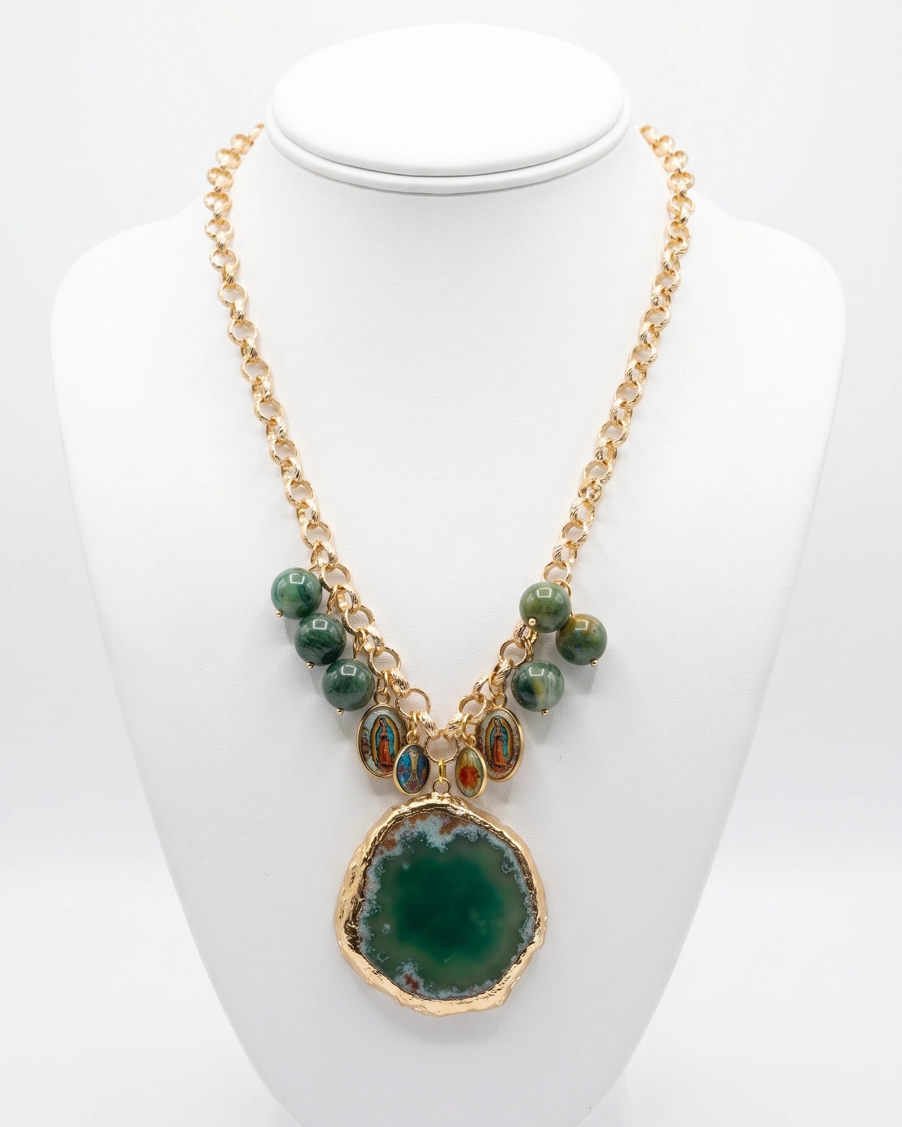 A gold-tone statement necklace displayed on a white mannequin bust. The necklace features a large green agate slice pendant, smaller green beads, and oval turquoise-like stone accents on a gold chain.