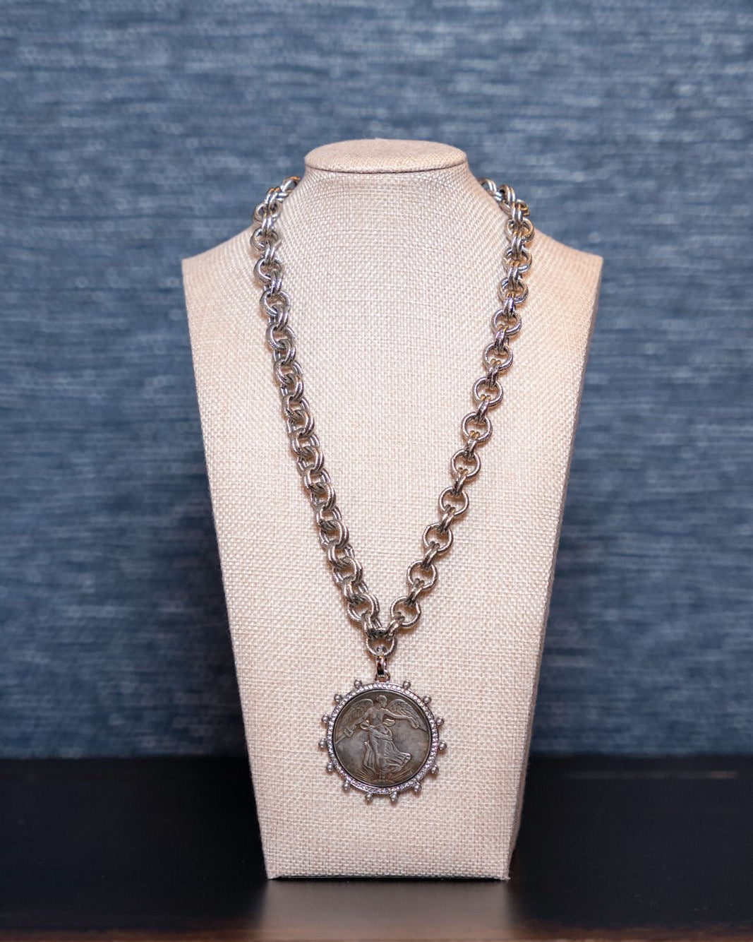 Long chain necklace with a pendant on a mannequin bust against a blue textured background