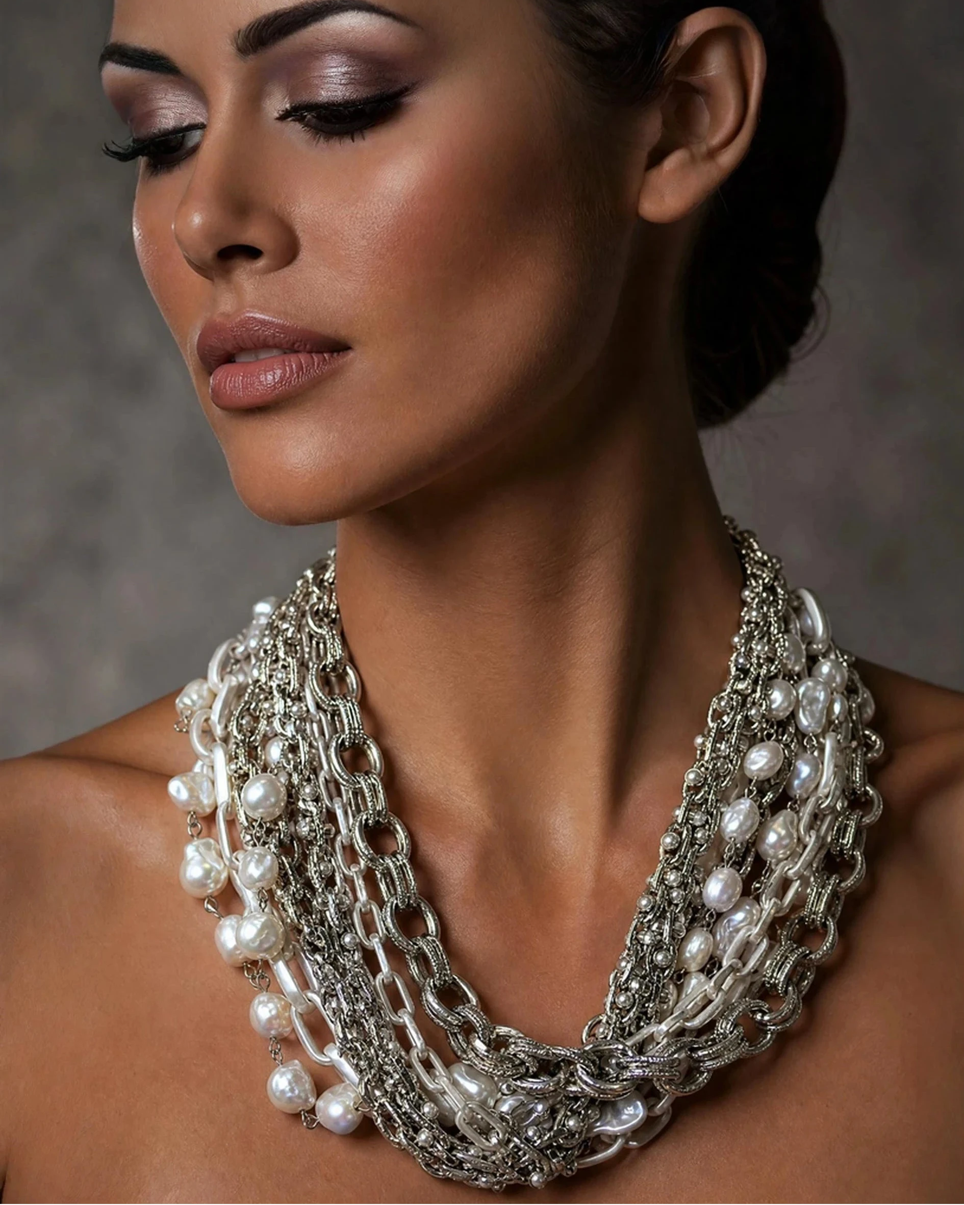 Woman wearing a layered silver and pearl necklace against a neutral background
