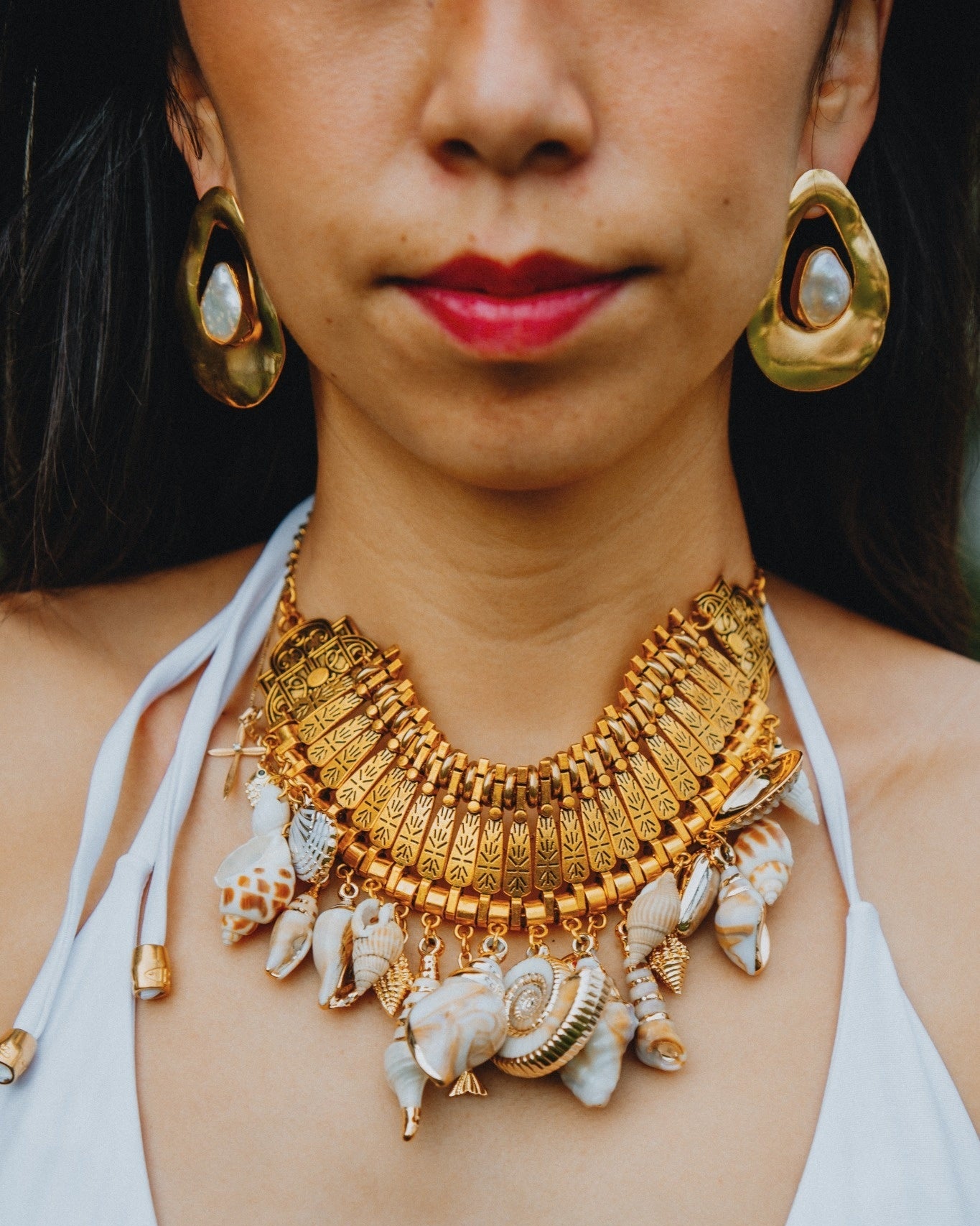 Woman wearing a gold necklace with shell accents and gold earrings.