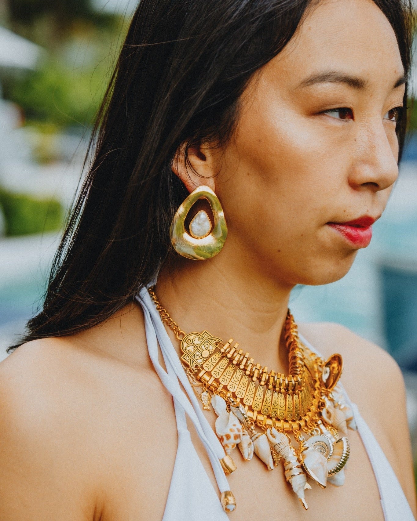 Woman wearing gold jewelry outdoors with blurred greenery in the background