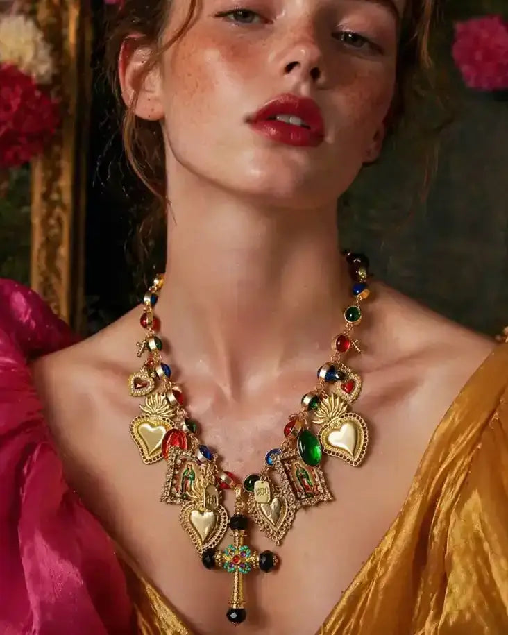 A close-up of a model wearing an ornate gold heart pendant necklace adorned with colorful gemstones, styled with a vibrant magenta and gold satin dress.