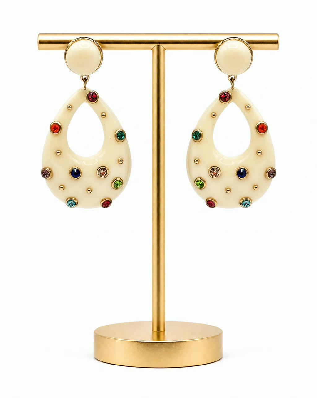 A pair of cream-colored teardrop dangle earrings decorated with colorful rhinestones and gold studs, displayed on a gold-colored jewelry stand against a white background.