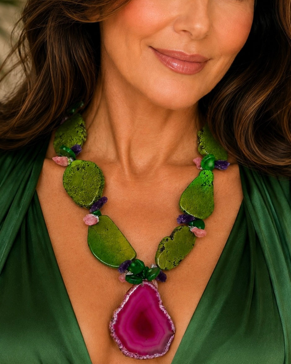A close-up of a woman wearing a green beaded necklace with a large magenta agate pendant, paired with a matching green satin top.