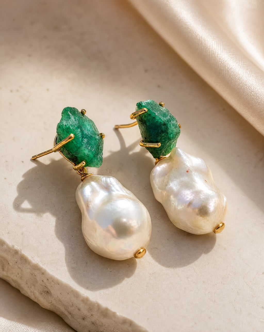 Pair of earrings with green gemstones and pearl-like stones on a beige surface